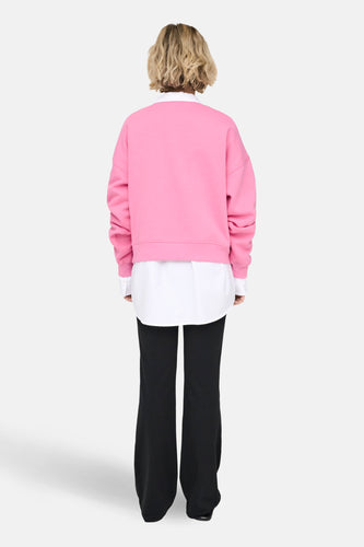 Achterkant van een vrouw met een roze trui, wit overhemd en zwarte broek.