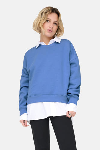Pull-over bleu d'ONLY, porté avec un chemisier blanc, un pantalon noir et des chaussures.