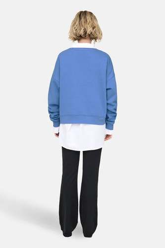 Pull-over bleu ONLY, avec des manches longues, porté sur une chemise blanche et un pantalon noir, dos.