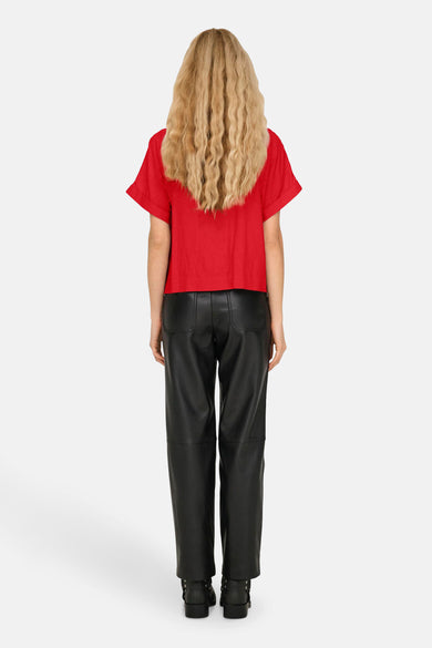 T-shirt rouge à manches courtes d'ONLY, avec un détail de pli sur la manche. Pantalon en cuir noir et bottes noires.