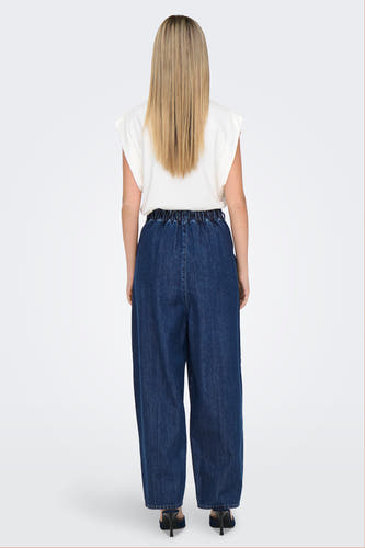 Donkerblauwe, wijde jeans van ONLY, met elastische tailleband en gedragen met een witte top en hakken.