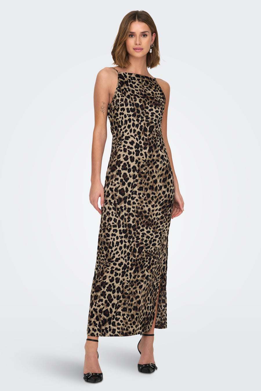 Vrouw in lange luipaardjurk met zwarte hakken staand voor witte achtergrond.
