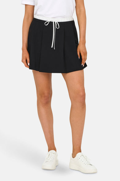 Jupe courte noire d'ONLY, avec une fermeture éclair à cordon blanc et portée avec des baskets blanches et un t-shirt blanc.