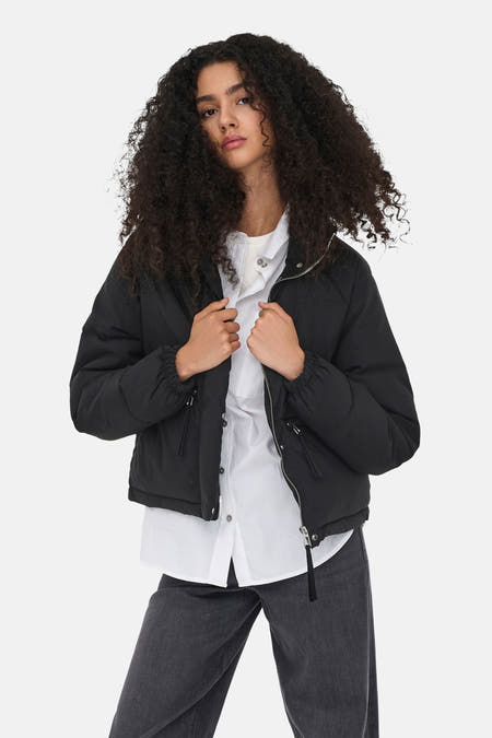 Manteau court noir de JDY porté sur une chemise blanche et un jean foncé.