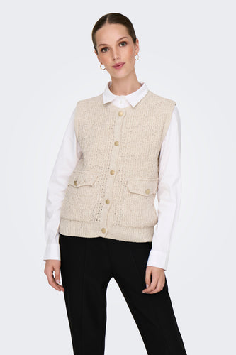 Vrouw met beige wollen vest over wit overhemd en zwarte broek.