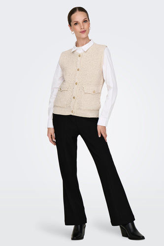 Vrouw met beige vest, wit overhemd en zwarte broek in studio.