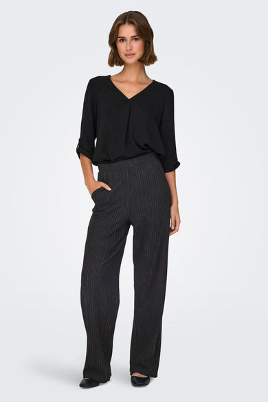 Zwarte broek van JDY, met krijtstreep en wijde pijpen, gecombineerd met een zwarte blouse.
