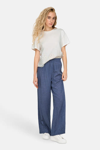 T-shirt blanc à manches courtes de JDY, avec des détails ajourés en bas et associé à un pantalon bleu.