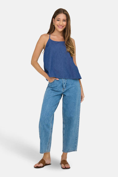Blouse en denim bleu sans manches de ONLY, avec des rubans spaghetti, associée à des jeans larges et des sandales brunes.