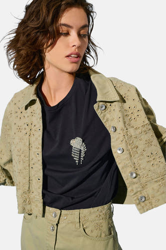 T-shirt beige à manches courtes de ONLY, avec une broche décorative et associé à un blouson kaki avec des broderies.