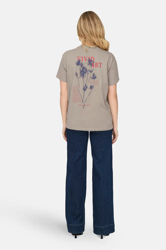 T-shirt beige à manches courtes de ONLY, avec des impressions rouges et bleues sur le dos, associé à des jeans foncés.