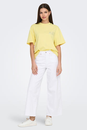 Geel T-shirt met korte mouwen van ONLY, met strass-opschrift, gecombineerd met een witte broek en sneakers.