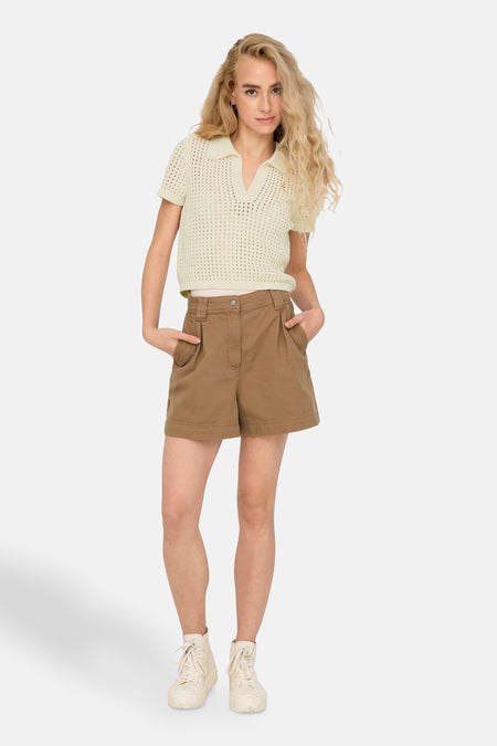 T-shirt écru ONLY, avec détail ouvert et porté avec des shorts bruns et des baskets blanches.
