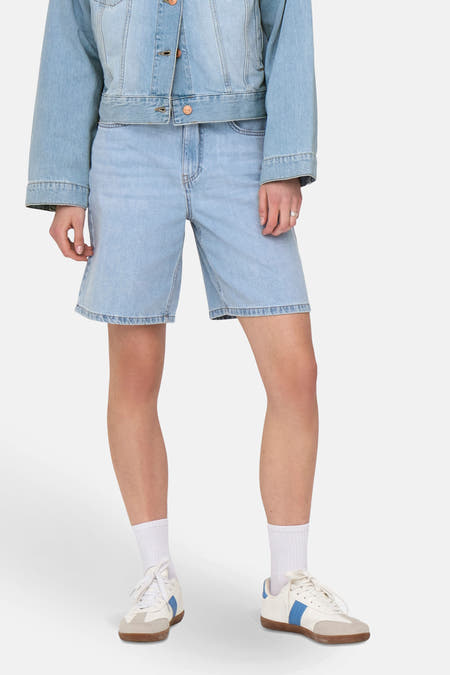 Short en denim bleu clair de ONLY, associé à une veste en jeans et des baskets blanches avec des détails bleus.
