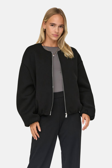 Manteau court noir de ONLY®, porté avec un haut gris et un pantalon noir, debout contre un fond blanc.