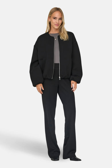 Zwarte korte jas van ONLY®, gedragen met een grijze top en zwarte pantalon, staand tegen een witte achtergrond.