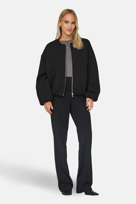 Zwarte korte jas van ONLY®, gedragen met een grijze top en zwarte pantalon, staand tegen een witte achtergrond.