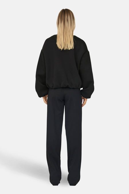 Manteau court noir d'ONLY, vu de derrière, combiné avec un pantalon noir.