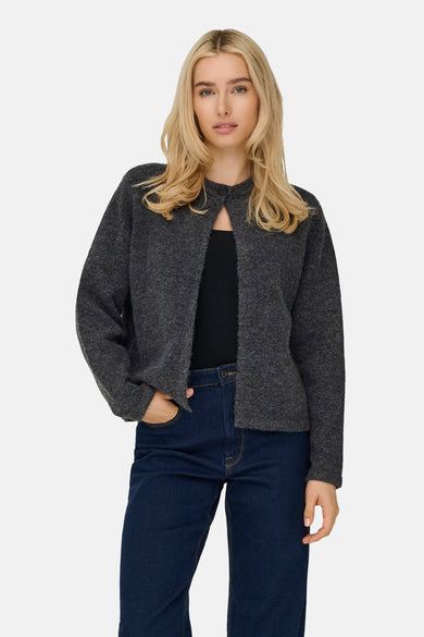 Femme aux cheveux blonds, cardigan gris et jeans bleus.
