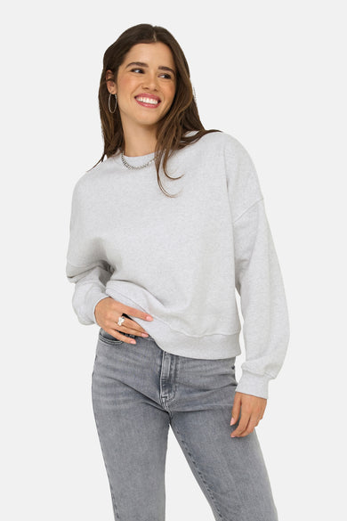 Pull-over gris ONLY, avec des manches longues et un col rond, associé à une chaîne argentée et des jeans gris.