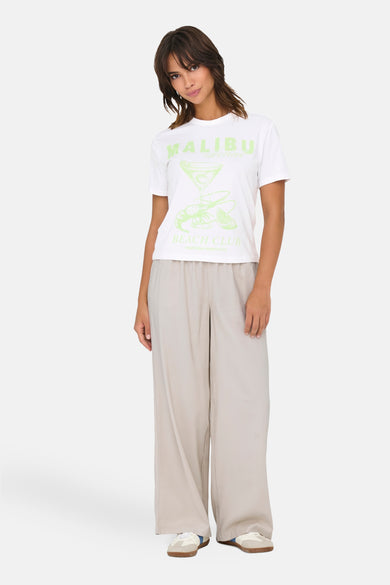 T-shirt blanc à manches courtes d'ONLY, avec une impression "Malibu Beach Club" verte claire, associé à un pantalon beige et des baskets.