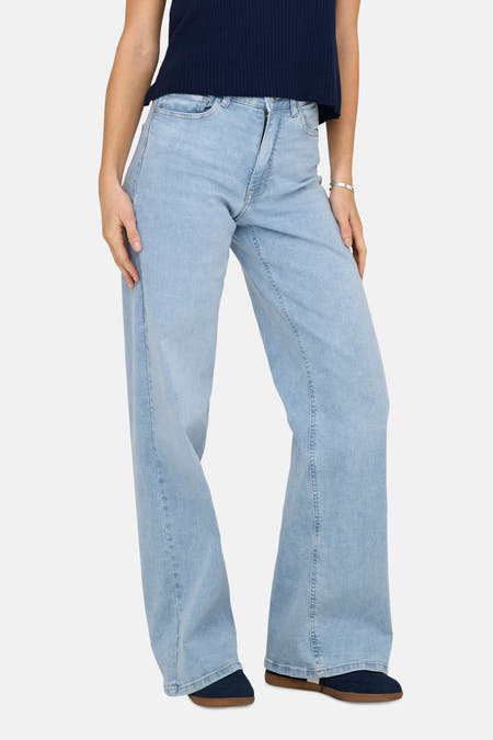 Jean bleu clair large de JDY, avec un bracelet en argent et une chemise bleu foncé.