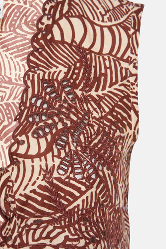 Detailopname van een bruin-beige kledingstuk met broderie en een patroon van bladeren.