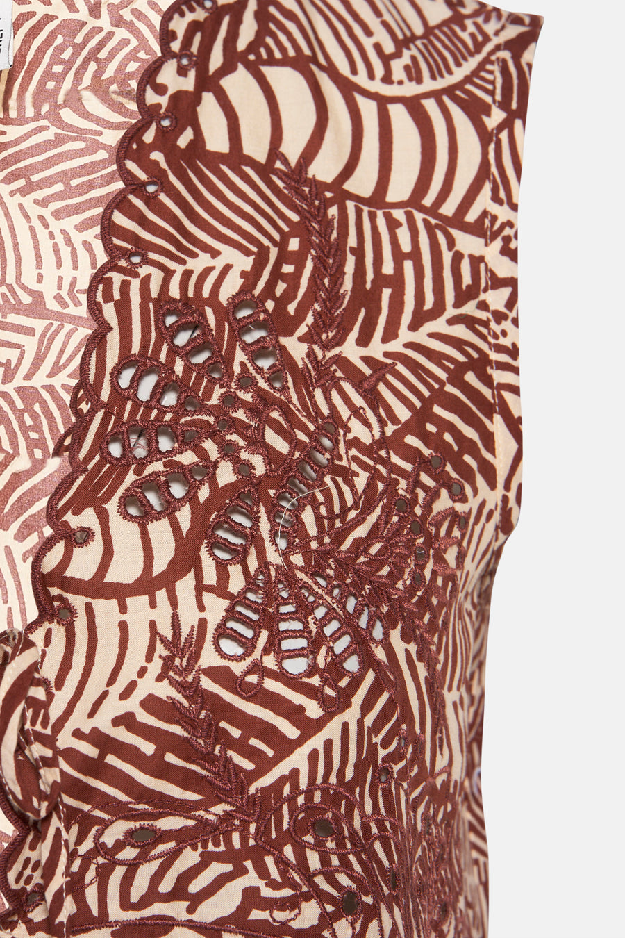 Detailopname van een bruin-beige kledingstuk met broderie en een patroon van bladeren.