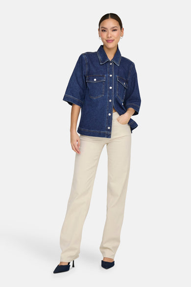 Chemise en denim bleu marine à manches courtes de ONLY®, portée avec un pantalon crème et des chaussures bleu marine.