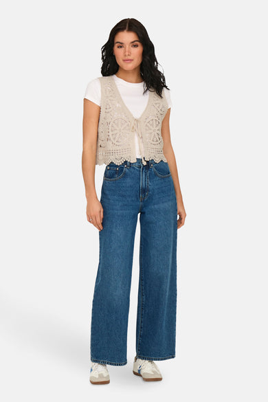 Gilet écru de JDY, porté sur un chemisier blanc et des jeans bleus larges.
