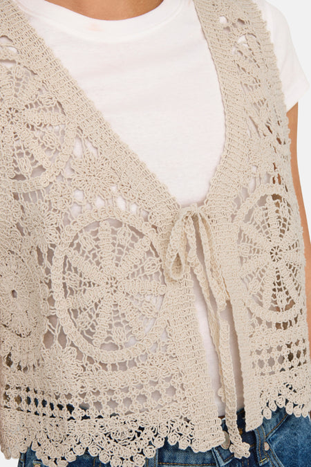 Gilet écru à mailles de JDY avec un motif floral tricoté et une fermeture à bouton, porté sur un t-shirt blanc.