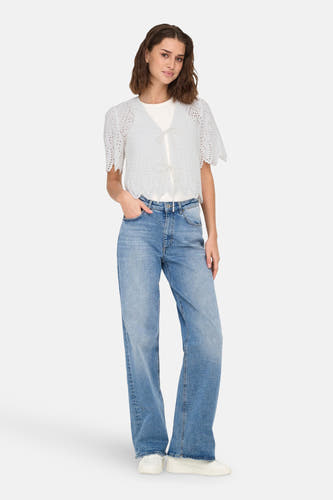 Blouse blanche à manches courtes de ONLY, avec des détails ajourés, portée avec des jeans et des baskets.