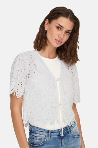 Blouse blanche à manches courtes de ONLY, avec des détails brodés et une fermeture éclair, portée avec un t-shirt blanc et des jeans bleus.