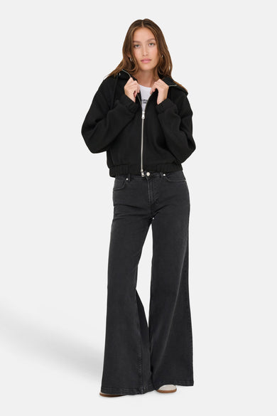 Manteau court noir d'ONLY, porté avec un T-shirt blanc et un jean noir à larges jambes.