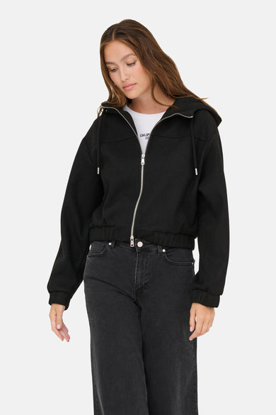 Manteau court noir d'ONLY, avec capuche et fermeture éclair argentée, porté avec un haut blanc et des jeans noirs.