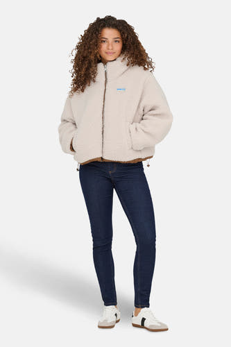 Manteau court écru de ONLY, avec des détails marrons et porté avec un jeans foncé et des baskets blanches.