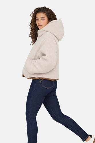 Manteau court écru d'ONLY, avec des bordures brunes et porté avec un jeans foncé.