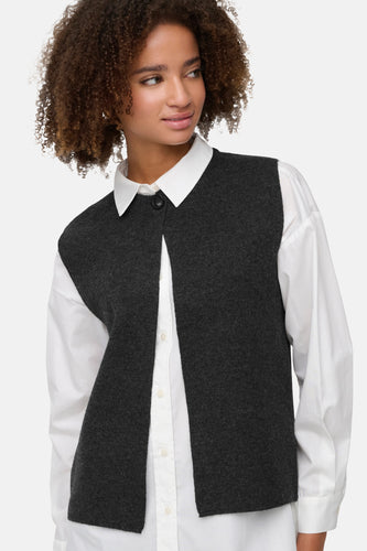 Vrouw in een witte blouse met een grijs vest.