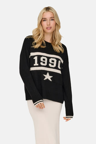 Pull-over noir à col rond de ONLY, avec des manches rayées, porté avec une jupe tricotée et des bottes en cuir.