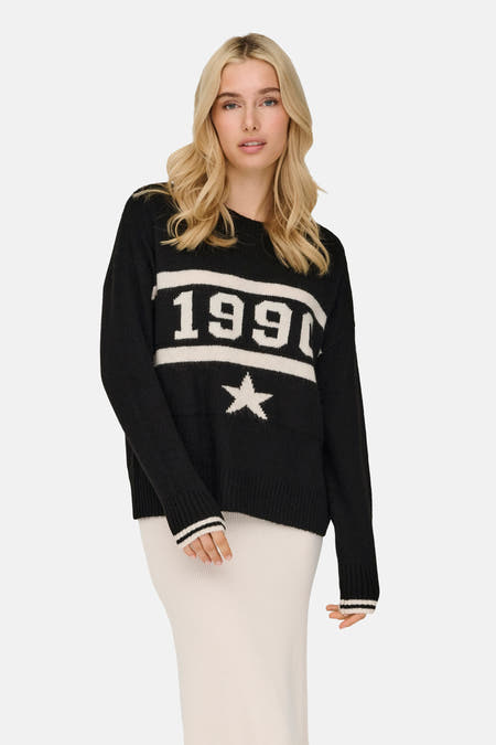 Pull-over noir à col rond de ONLY, avec des manches rayées, porté avec une jupe tricotée et des bottes en cuir.