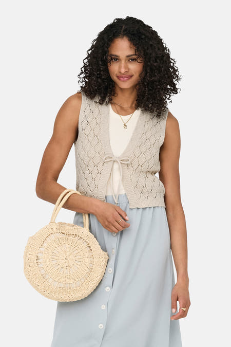 Gilet écru de ONLY, avec un motif de tricot ouvert, une fermeture à glissière et associé à une jupe bleue et un panier en paille.