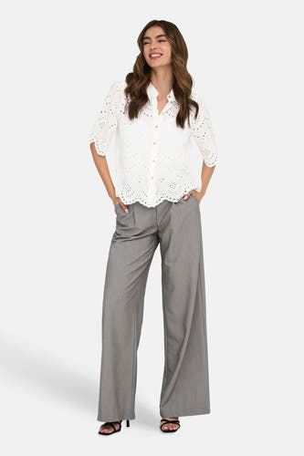 Wit hemd van ONLY met broderie details, gedragen met een grijze pantalon en zwarte sandalen.
