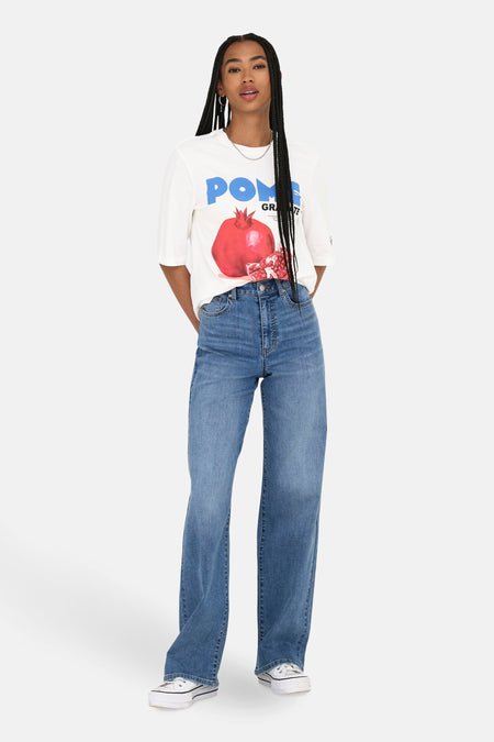 T-shirt blanc à manches courtes de ONLY, avec imprimé pomme de grenade, associé à des jeans larges et des baskets blanches.