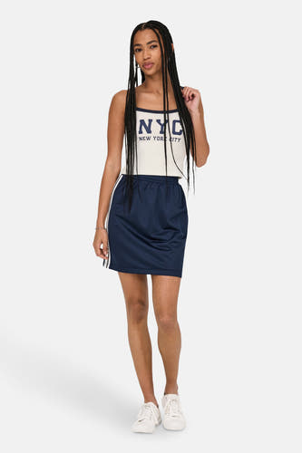 T-shirt blanc ONLY®, avec une impression bleu marine NYC et porté avec une jupe marine et des baskets blanches.