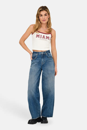T-shirt blanc ONLY, avec finition rouge et texte "Miami Florida", porté avec des jeans larges et des chaussures noires.