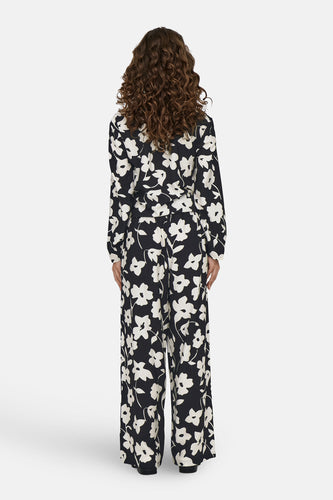 Vrouw met krullend haar, bloemenprint jumpsuit, achterkant, witte achtergrond.
