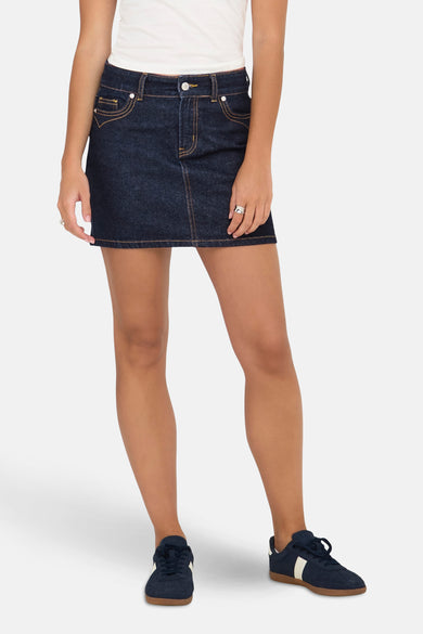 Short skirt of dark blue denim from ONLY, with a yellow stitch and combined with a white top and blue sneakers.