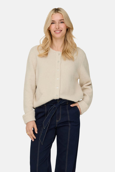 Veste écru de ONLY, avec des manches longues, une fermeture à boutons et portée avec un pantalon bleu marine à ceinture.