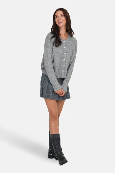 Grijze cardigan van ONLY, gedragen met een geruite minirok en zwarte laarzen met sokken.
