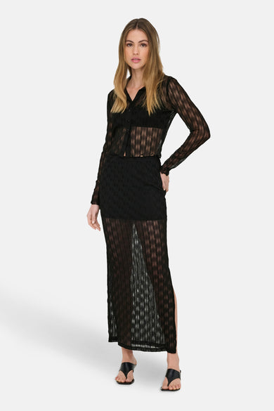T-shirt noir à manches longues de ONLY, avec une texture transparente et porté avec une jupe noire et des bottes.